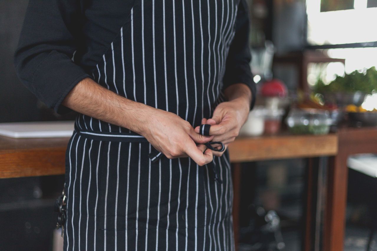 Person wearing a black kitchen apron with white stripes in a kitchen setting