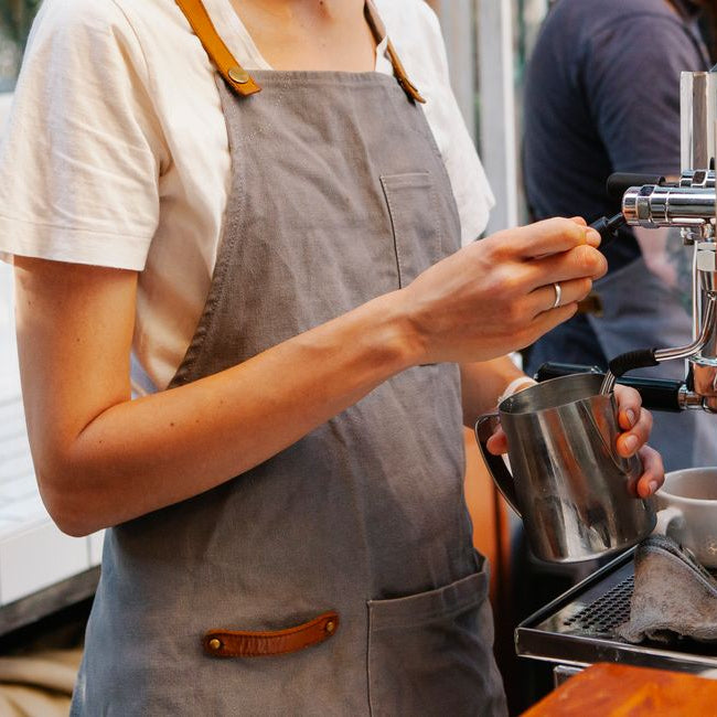 Person in a grey staff apron operating a coffee machine